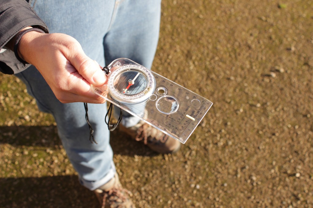 Image of a compass being held in someone's hand - you can see their legs and feet in the background